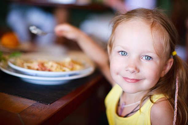 Image of a young girl smiling at the camera and eating a bowl of pasta. Kids eat free February half term 2024