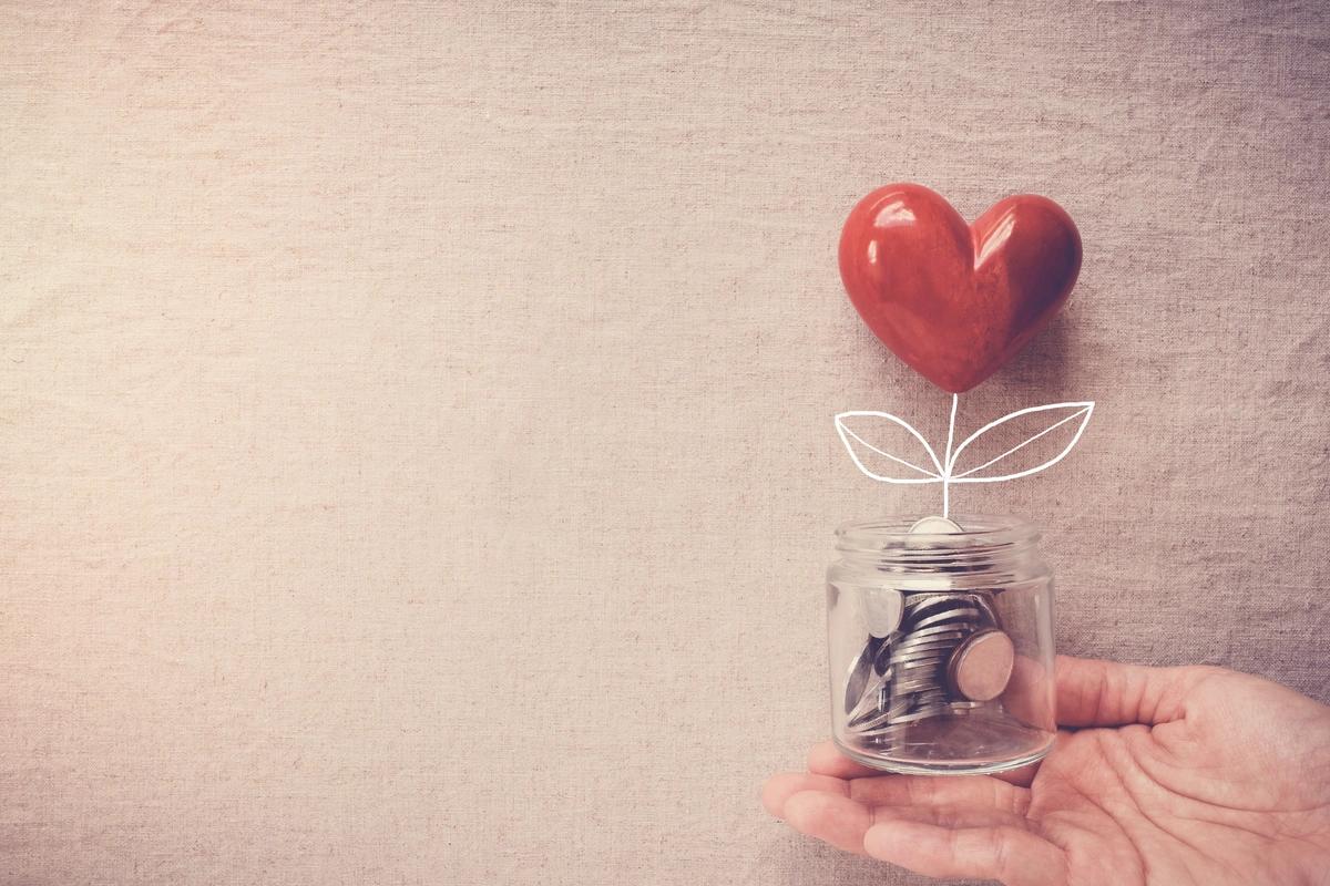 Hand holding a jar of coins with a heart flower growing out of it