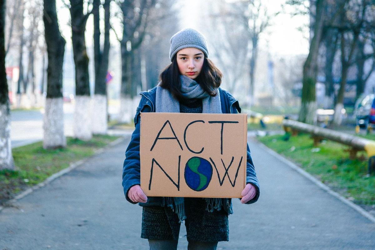 A woman holding a protest banner about climate change that says 'Act now'