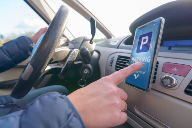Image of a man inside a car with a mobile phone mounted on the dash board selecting a parking app