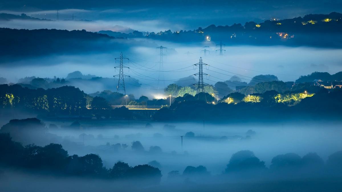 Electricity pylons in a misty valley at night