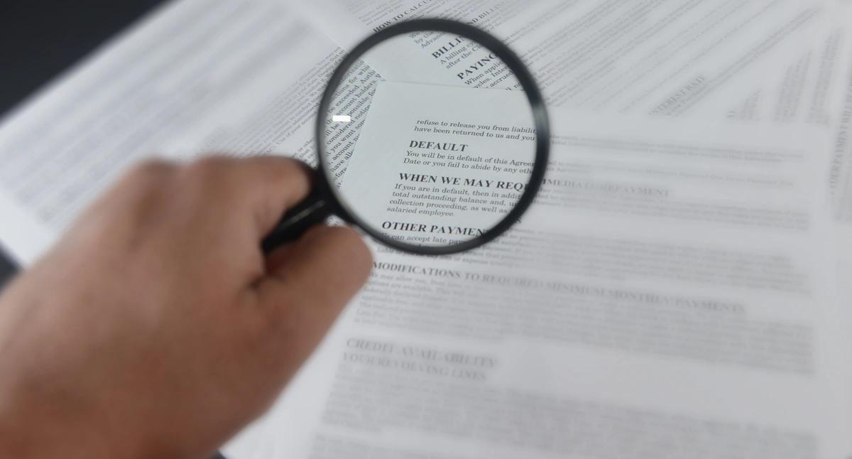 A hand holds a magnifying glass over information on default in a bank letter