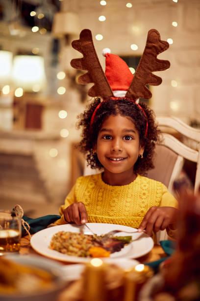 Image of a little girl with reindeer antler headband eating a meal and looking happy