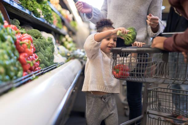 Image of a chime picking up some broccoli and putting it in her mum's supermarket trolly