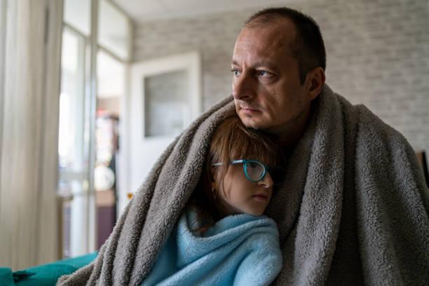 Image of a man cuddling his daughter with blankets around them in a cold home